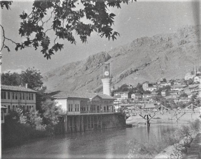 1937'de Yeşilırmak kıyısı: kayanın üstünde saat kulesi, sağda ahşap köprü, kıyıda ahşap direkler üzerine oturan binalar