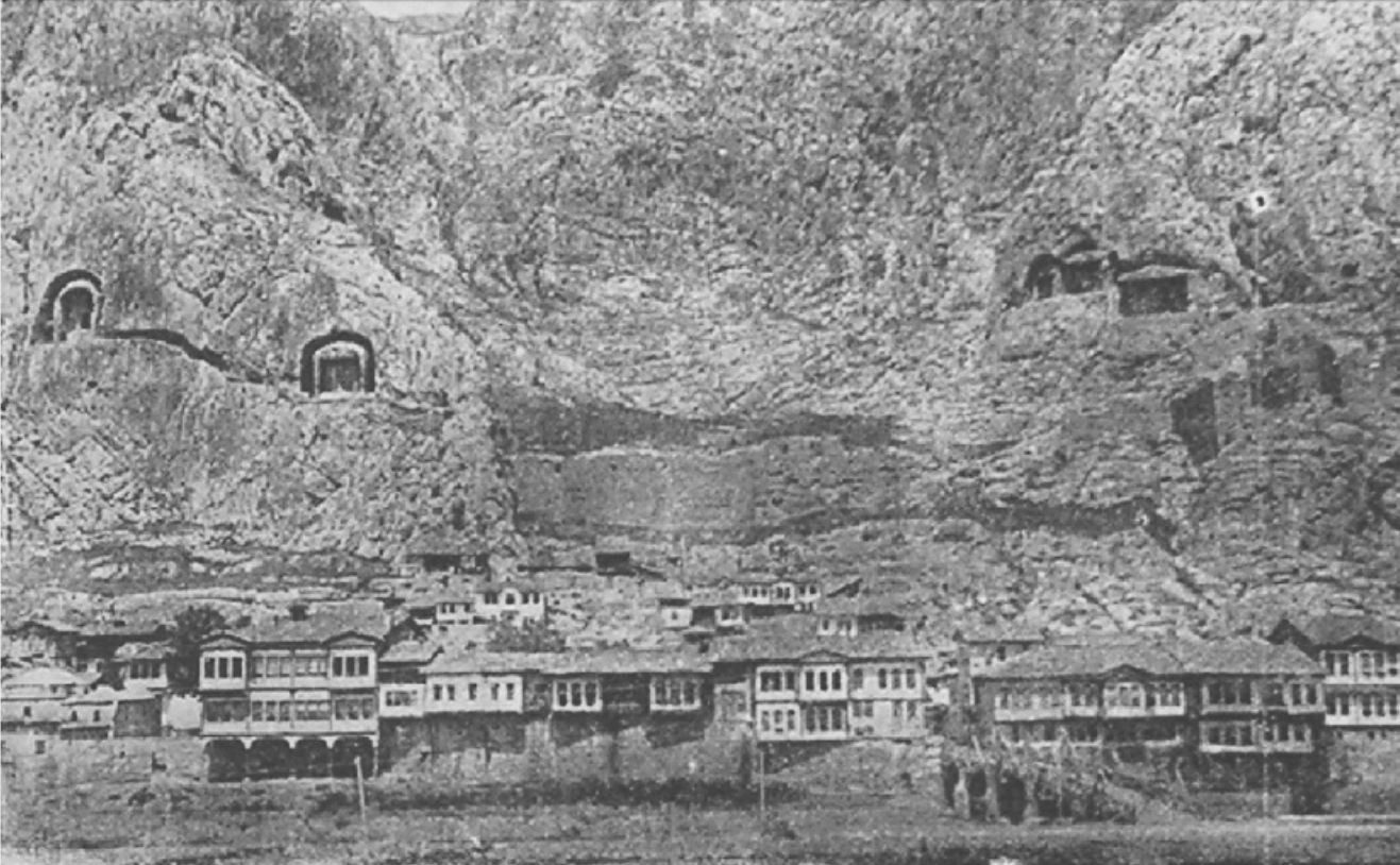 Kaya yüzünün altında, ırmak kıyısında sıra sıra dizilmiş çıkmalı ahşap evler; yukarıda kayaya oyulmuş kral mezarları